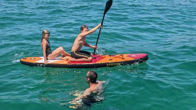 Image of kids paddle boarding while a man is swimming